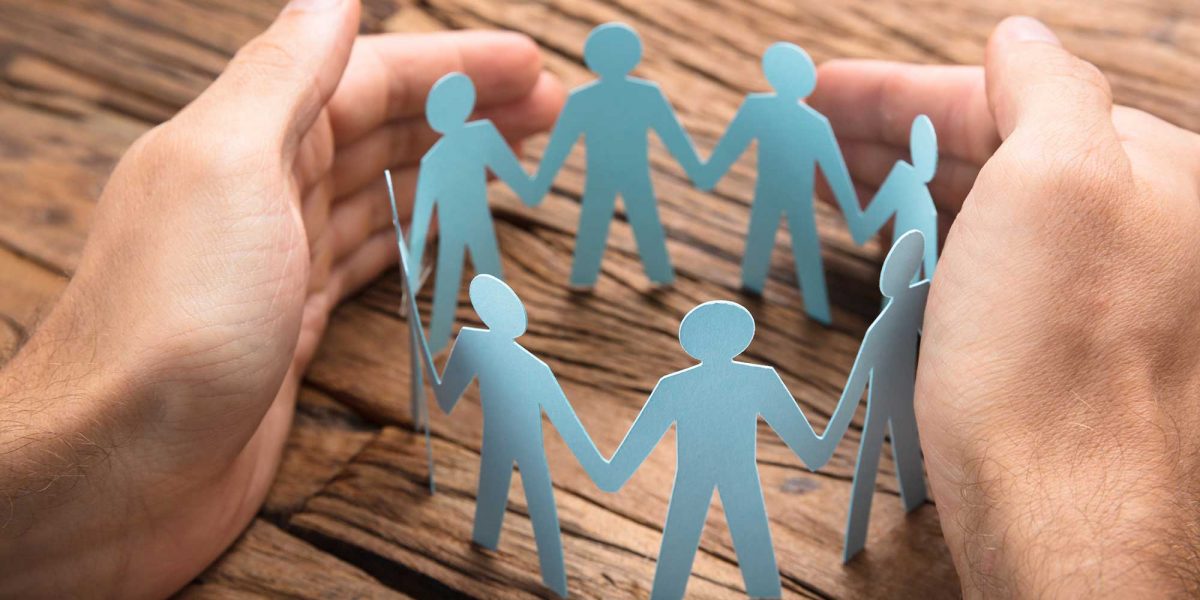 Cropped image of businessman's hands covering paper team on wooden table